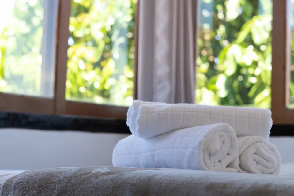Toalhas enroladas sobre a cama, com janela para o jardim